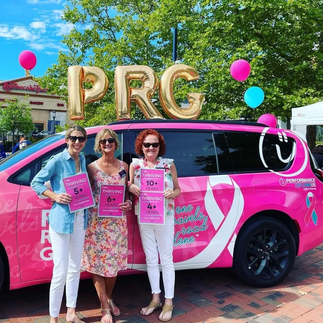 Women smiling holding up signs next to a van 